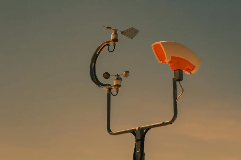 Weather station with anemometer and wind vane mounted on a pole against a warm sunset sky, used for renewable energy monitoring