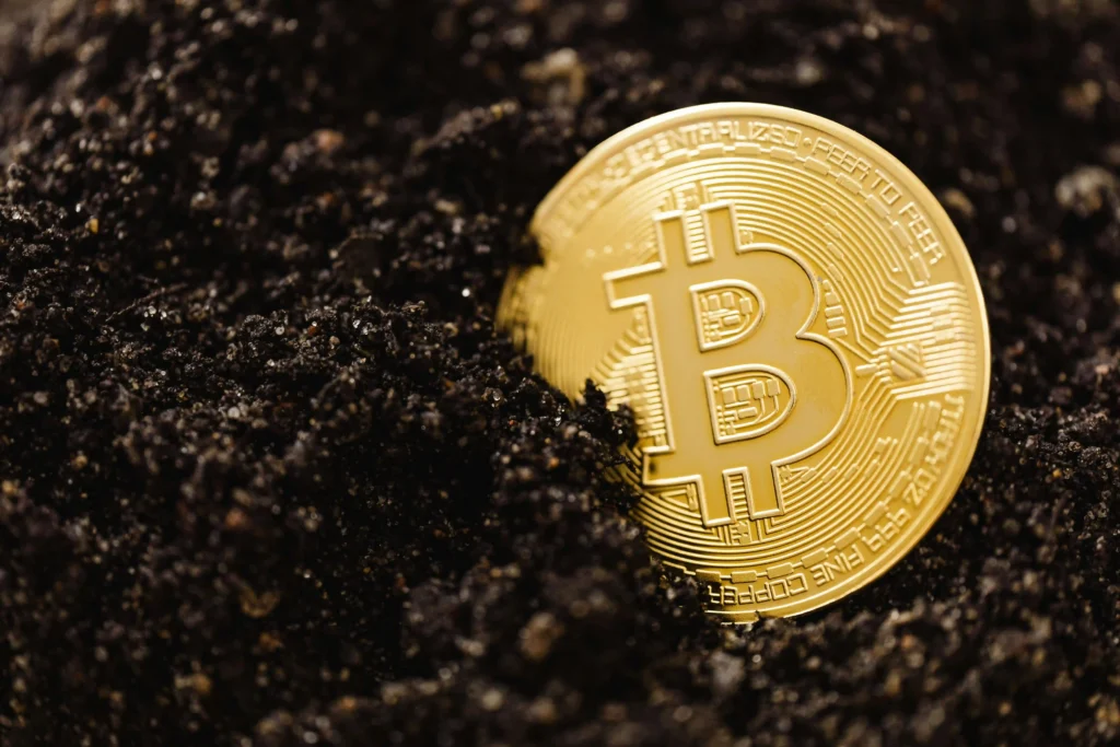 Golden Bitcoin coin partially buried in dark soil, close-up macro shot