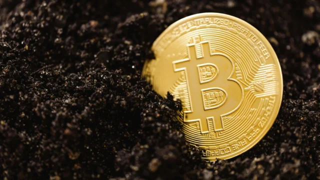 Golden Bitcoin coin partially buried in dark soil, close-up macro shot