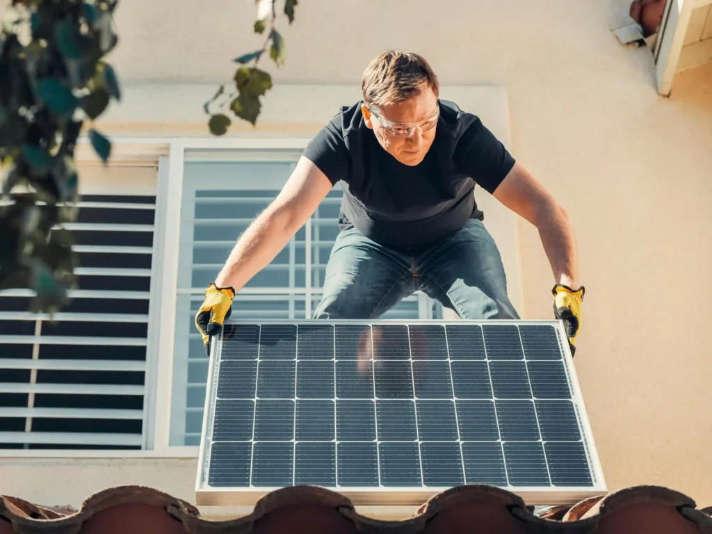 Technician wearing safety glasses and yellow gloves installing a solar panel on a residential rooftop