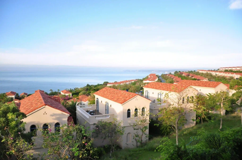 Aerial view of Mediterranean-style villas with terracotta roofs nestled in lush greenery overlooking the sea