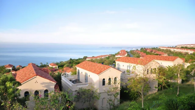 Aerial view of Mediterranean-style villas with terracotta roofs nestled in lush greenery overlooking the sea