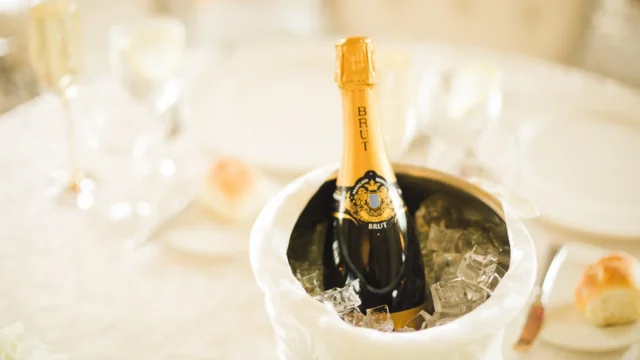 Brut champagne bottle chilling in an ice bucket on an elegantly set dining table with glasses in soft bokeh light