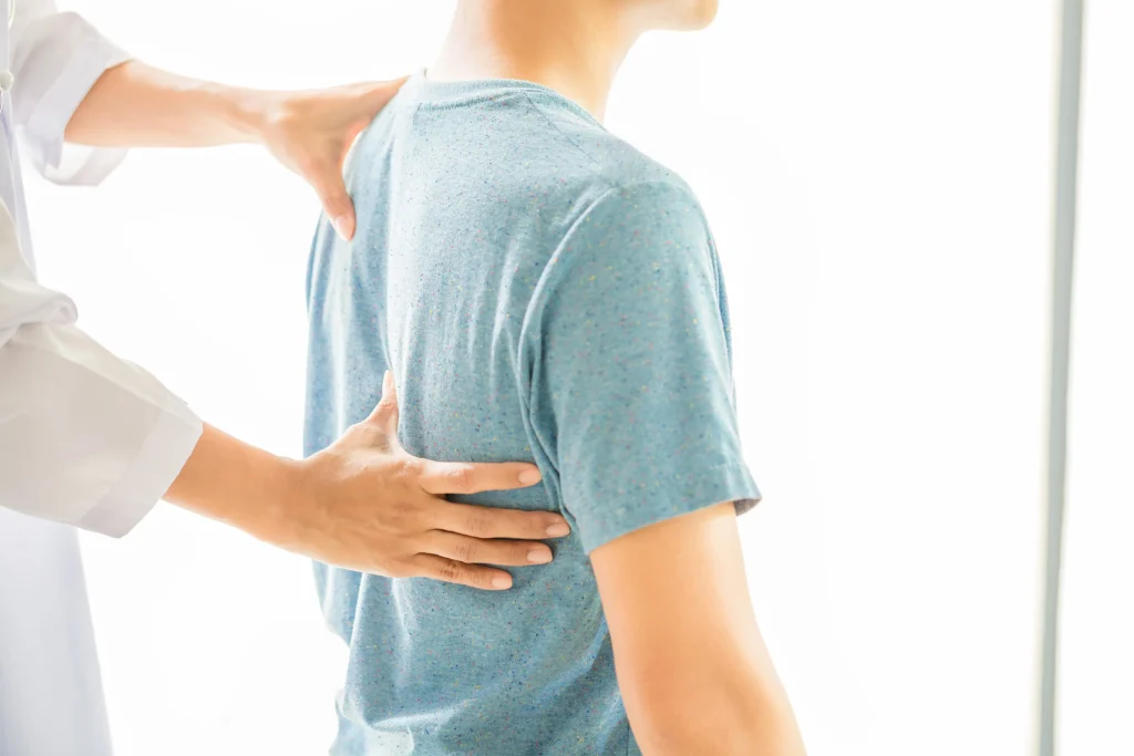 Chiropractor examining a patient's back with both hands in a bright white clinical setting, close-up view