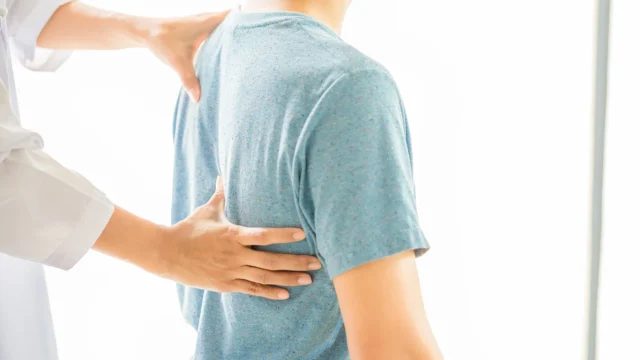 Chiropractor examining a patient's back with both hands in a bright white clinical setting, close-up view