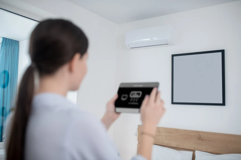 Woman adjusting a smart air conditioning control panel in a bright room with a wall-mounted AC unit