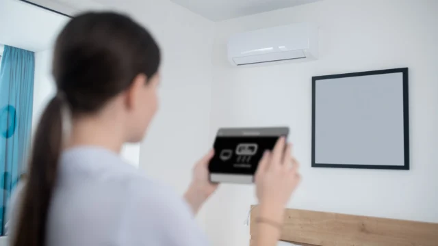 Woman adjusting a smart air conditioning control panel in a bright room with a wall-mounted AC unit