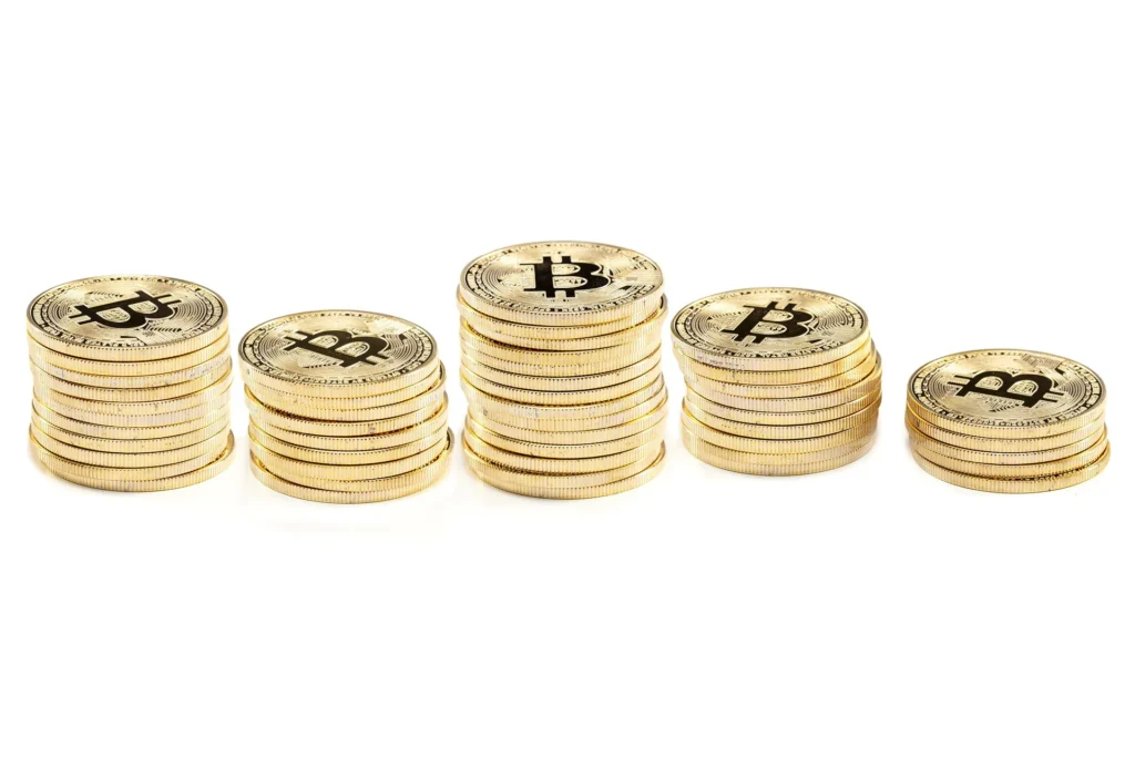 Five stacks of gold Bitcoin coins of varying heights arranged in a row on a white background