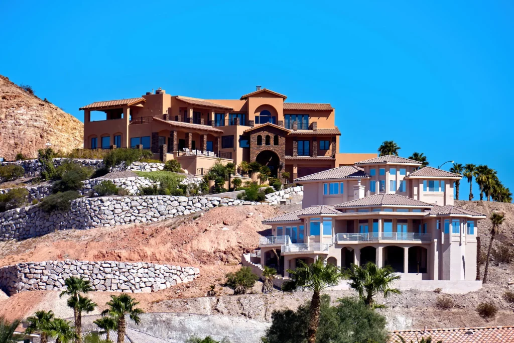 Luxury Mediterranean-style hotel buildings on a hillside with stone terraces and palm trees under a bright blue sky
