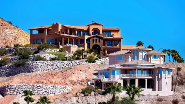 Luxury Mediterranean-style hotel buildings on a hillside with stone terraces and palm trees under a bright blue sky