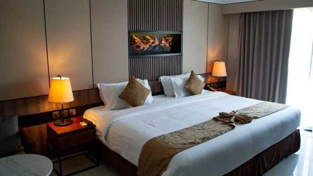 Elegantly furnished hotel room with a king-size bed, warm bedside lamps, wood paneling and decorative artwork above the headboard
