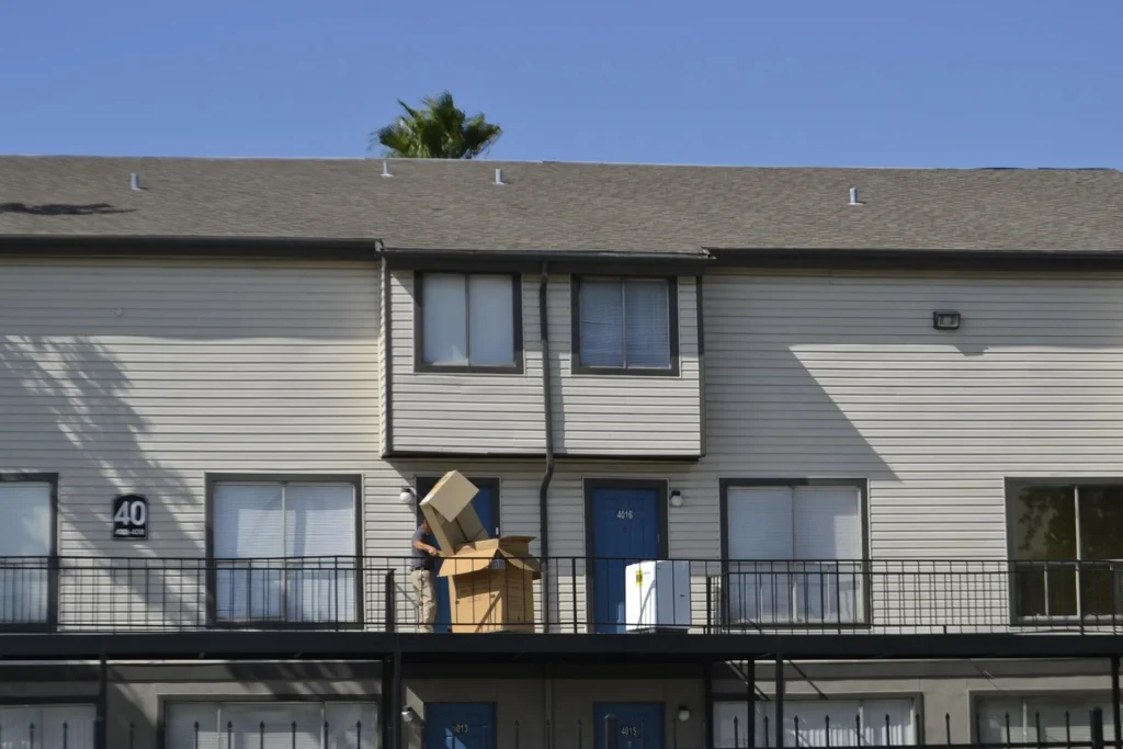 Person carrying cardboard moving boxes on the balcony of a residential apartment building on a sunny day