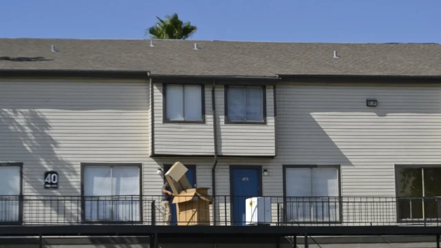 Person carrying cardboard moving boxes on the balcony of a residential apartment building on a sunny day
