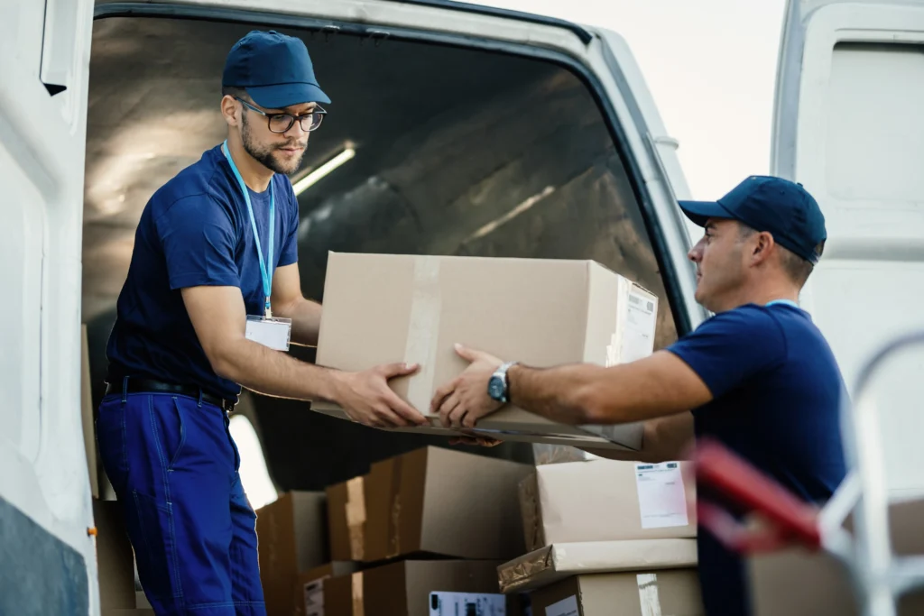 Two professional movers in blue uniforms unloading cardboard boxes from a delivery van