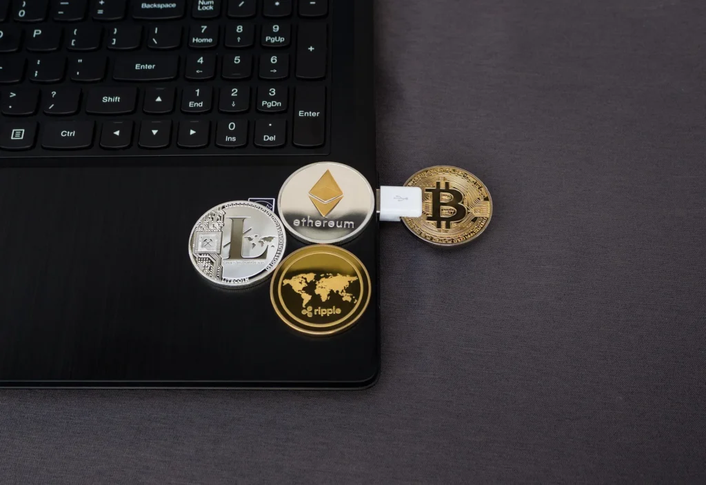 Physical cryptocurrency coins including Bitcoin, Ethereum, Litecoin and Ripple placed on a laptop keyboard with a USB connector