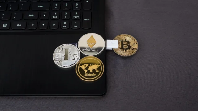 Physical cryptocurrency coins including Bitcoin, Ethereum, Litecoin and Ripple placed on a laptop keyboard with a USB connector